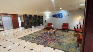 Eine Lobby mit gemustertem Teppich, gefliestem Boden, Steinwand und einer Sitzecke mit Stühlen und einem kleinen Tisch.