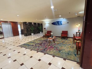 Un hall con alfombra estampada, suelo de baldosas, pared de piedra y zona de estar con sillas y una mesa pequeña.