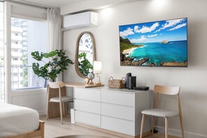Habitación de hotel moderna con una cama, un escritorio con una silla, un ventanal con cortinas, una planta en maceta, un globo terráqueo, una lámpara, una cesta tejida y un cuadro con una imagen de playa.