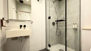 Ein modernes Badezimmer mit einer gläsernen Duschkabine, einem weißen Waschbecken mit schwarzem Wasserhahn und einem Spiegel über dem Waschbecken.