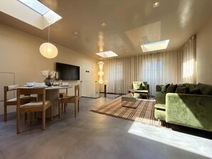 A modern living room with a dining area, a sofa, a TV, and a large window with curtains. - Exclusive 3BR Duplex – Notting Hill & Holland Park (Greater London)