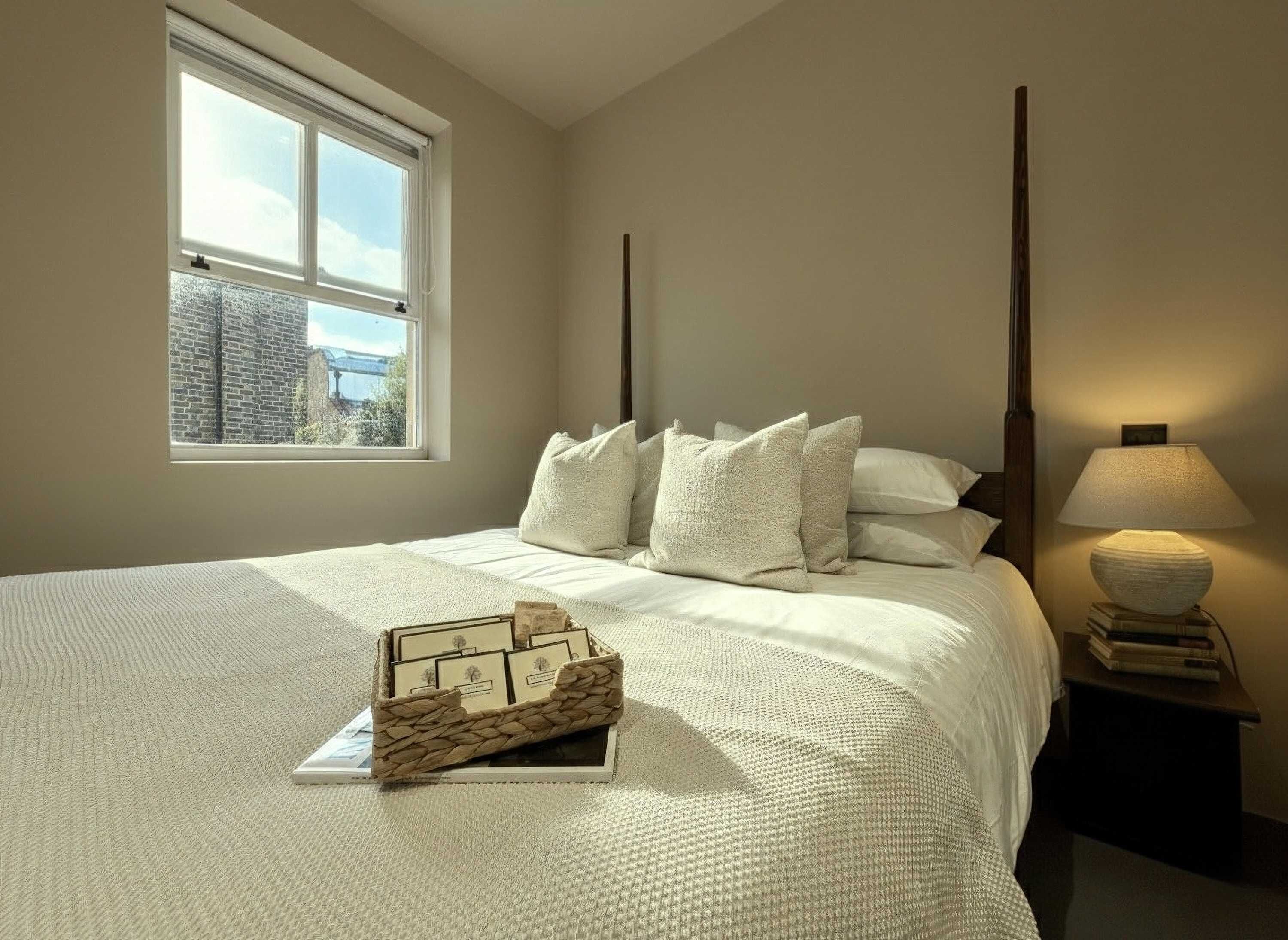 A bedroom with a large bed, a window with a view of a building, a bedside lamp, and a decorative box on the bed.