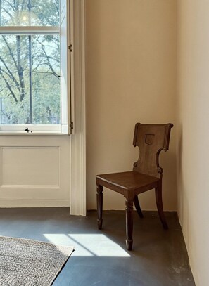 Ein Zimmer mit einem Holzhocker, einem Fenster mit Blick auf Bäume und einer Tür.