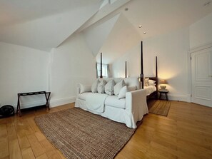 Ein Zimmer mit einer weißen Couch, einem Bett, einer Stehlampe und Holzboden.