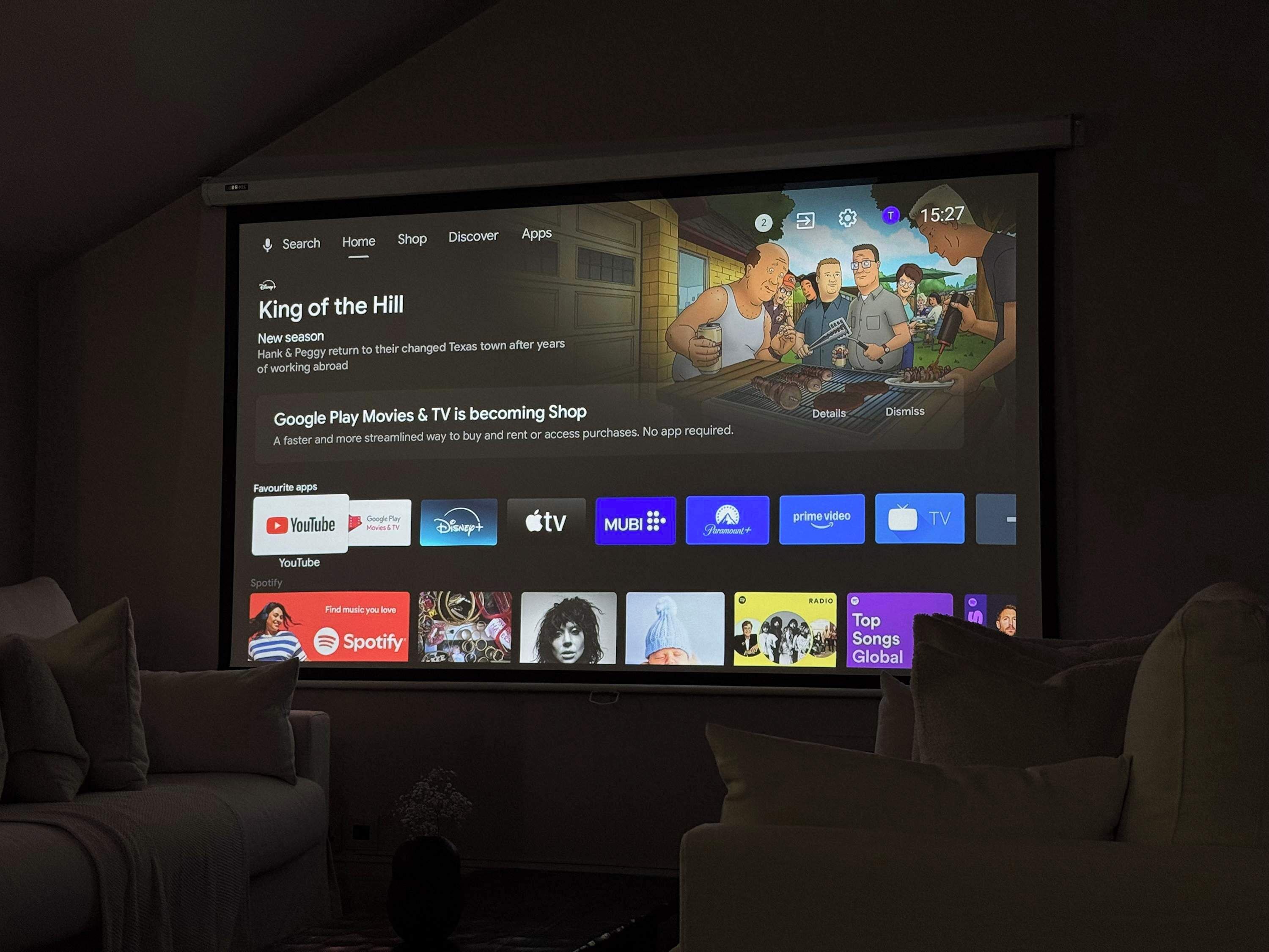 A television screen displaying a streaming service interface with a menu bar, a featured show, and various app icons.
