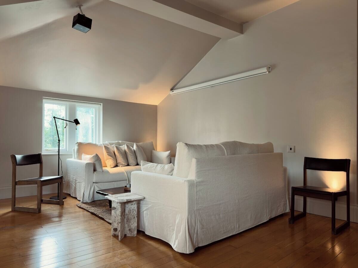 Een moderne woonkamer met een witte bank, twee houten stoelen, een klein bijzettafeltje en een vloerlamp.