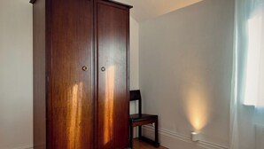 A room with a wooden wardrobe, a chair, and a window with curtains. - Grand 2BR Penthouse | 100" Cinema | Hyde Park (London)
