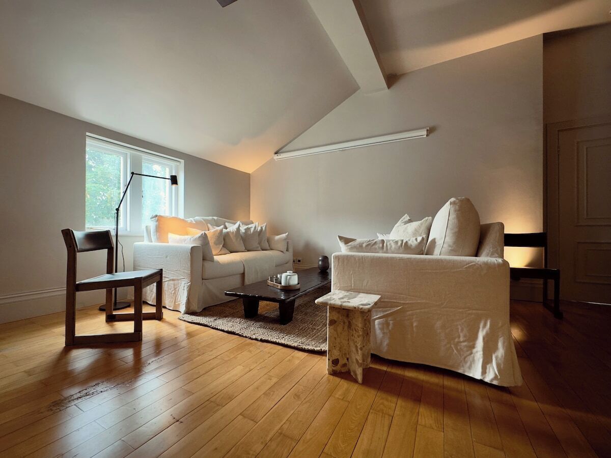 Een ruime woonkamer met een hoge plafond, een groot raam en een houten vloer.