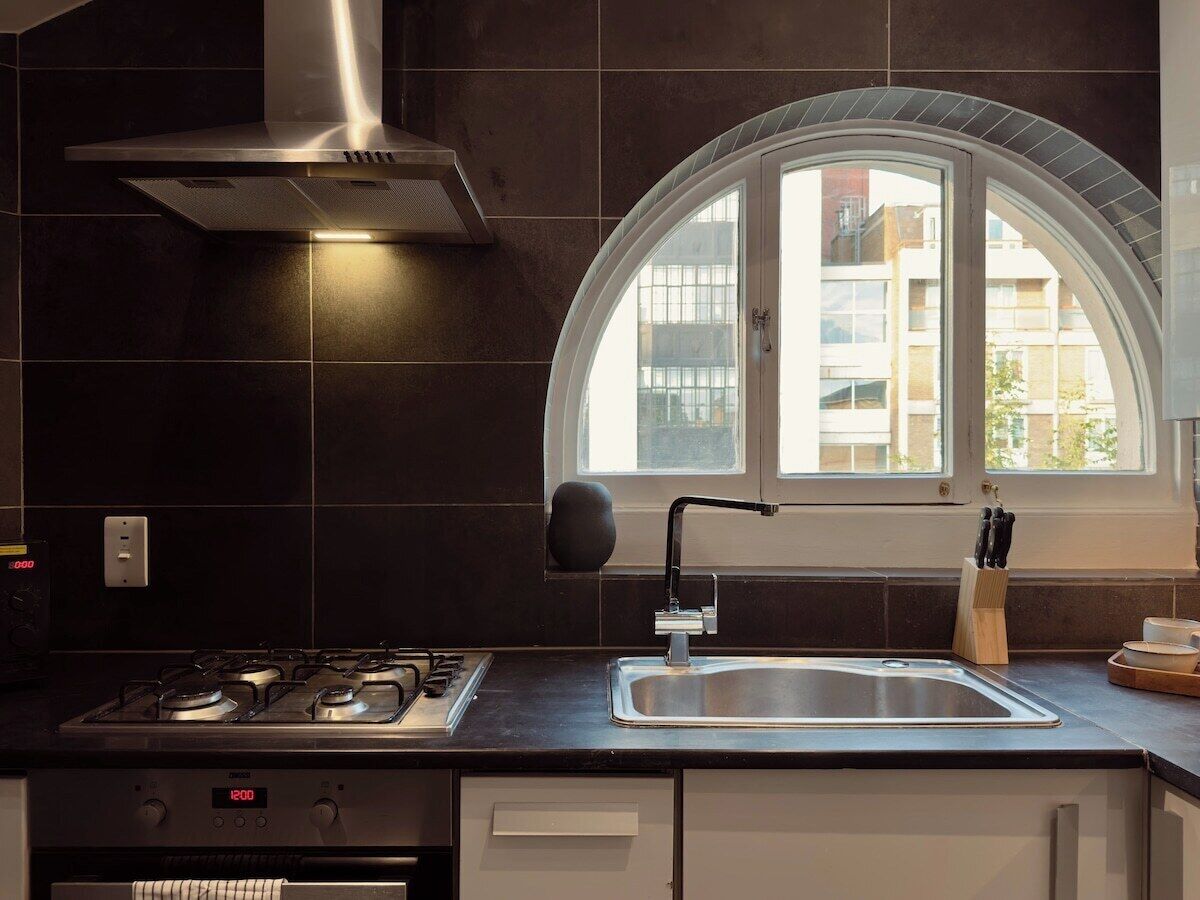 A modern kitchen with a gas stove, stainless steel sink, and a window with a view of buildings.