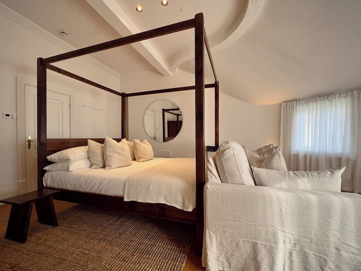 A four-poster bed with a wooden frame, a bedside table, and a large mirror on the wall.