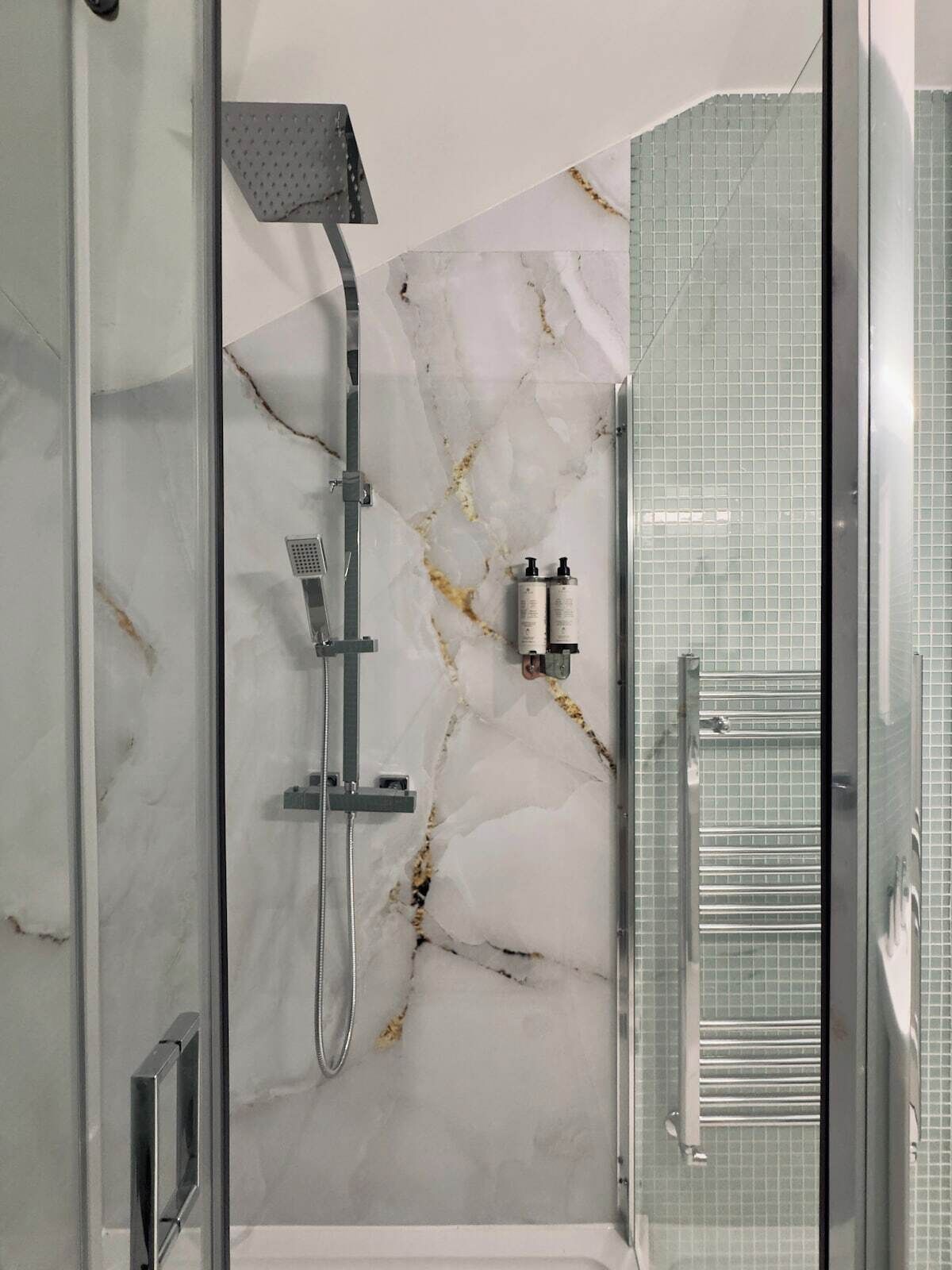 A modern bathroom with a glass-enclosed shower, marble walls, and a glass door.