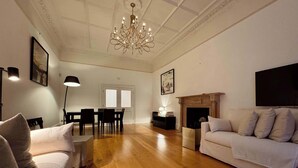 Ein geräumiges Wohnzimmer mit einer Chandelieber, einem Kamin, einer Couch und einem Essbereich.