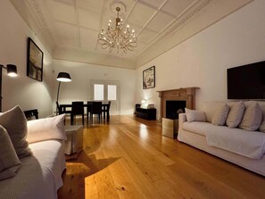 Ein geräumiges Wohnzimmer mit einer Chandelieber, einem Kamin, einer Couch und einem Essbereich.