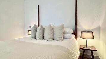 A bedroom with a bed, pillows, a bedside table with a lamp, and a wooden floor.