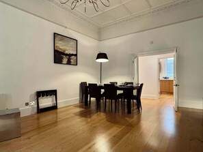 A dining area with a table and chairs, a painting on the wall, and a chandelier. - Grand South Ken Sanctuary | Fire Place | Courtyard (London)