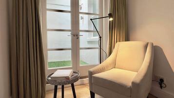 A room with a white armchair, a small round table with a book, a floor lamp, and a glass door leading outside.