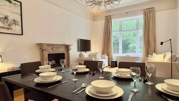 A dining room with a long table set for a meal, a fireplace, a sofa, and a large window with curtains.