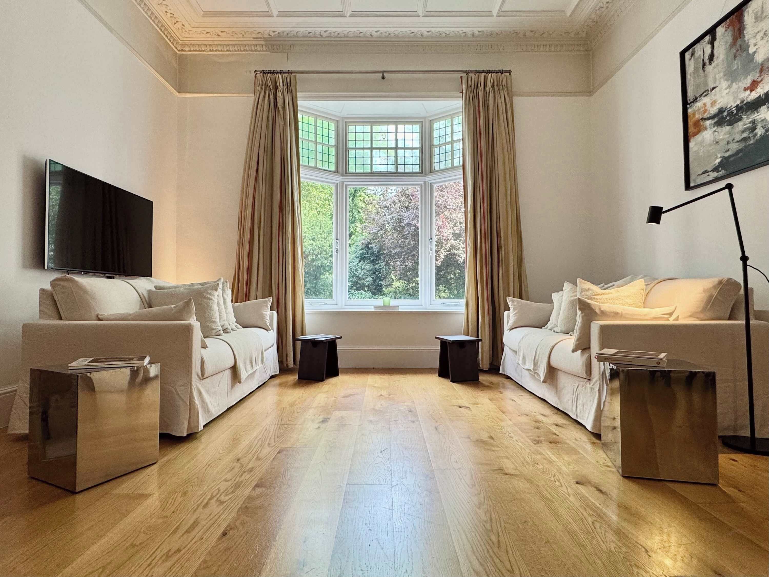 Sala de estar com dois sofás, uma televisão, luminária de chão e uma janela grande com cortinas.