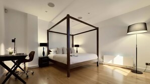Ein Schlafzimmer mit Himmelbett, Schreibtisch, Stuhl, Stehlampe und Heizkörper.