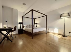 Ein Schlafzimmer mit Himmelbett, Schreibtisch, Stuhl, Stehlampe und Heizkörper.