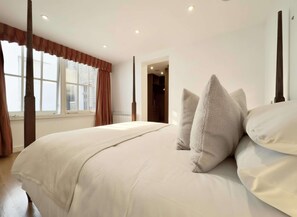 A bedroom with a large bed, a window with curtains, a radiator, and a door leading to another room. - Grand South Ken Sanctuary | Fire Place | Courtyard (London)