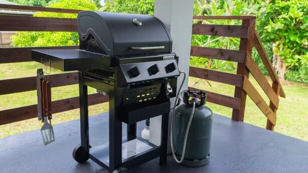 A portable grill with a gas tank on a table, outdoors with a wooden fence and greenery in the background. - Tropical Moorea Escape, 3BR, A/C, Strong WiFi & Mountain Views (Moorea-Maiao)
