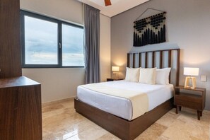 A hotel room with a large bed, a nightstand, a wall-mounted lamp, and a window with curtains. - Luxury 2 BR PH w/Private Pool, Walk to Beach (Tulum)