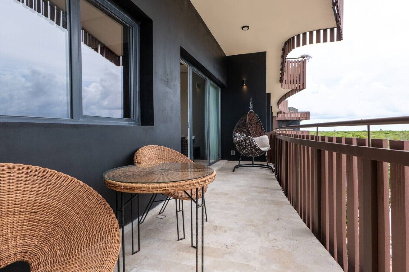 A balcony with wicker furniture, a hanging chair, and a view of the landscape.