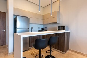 A modern kitchen with a white countertop, stainless steel appliances, and two black bar stools. - Luxury 2 BR PH w/Private Pool, Walk to Beach (Tulum)