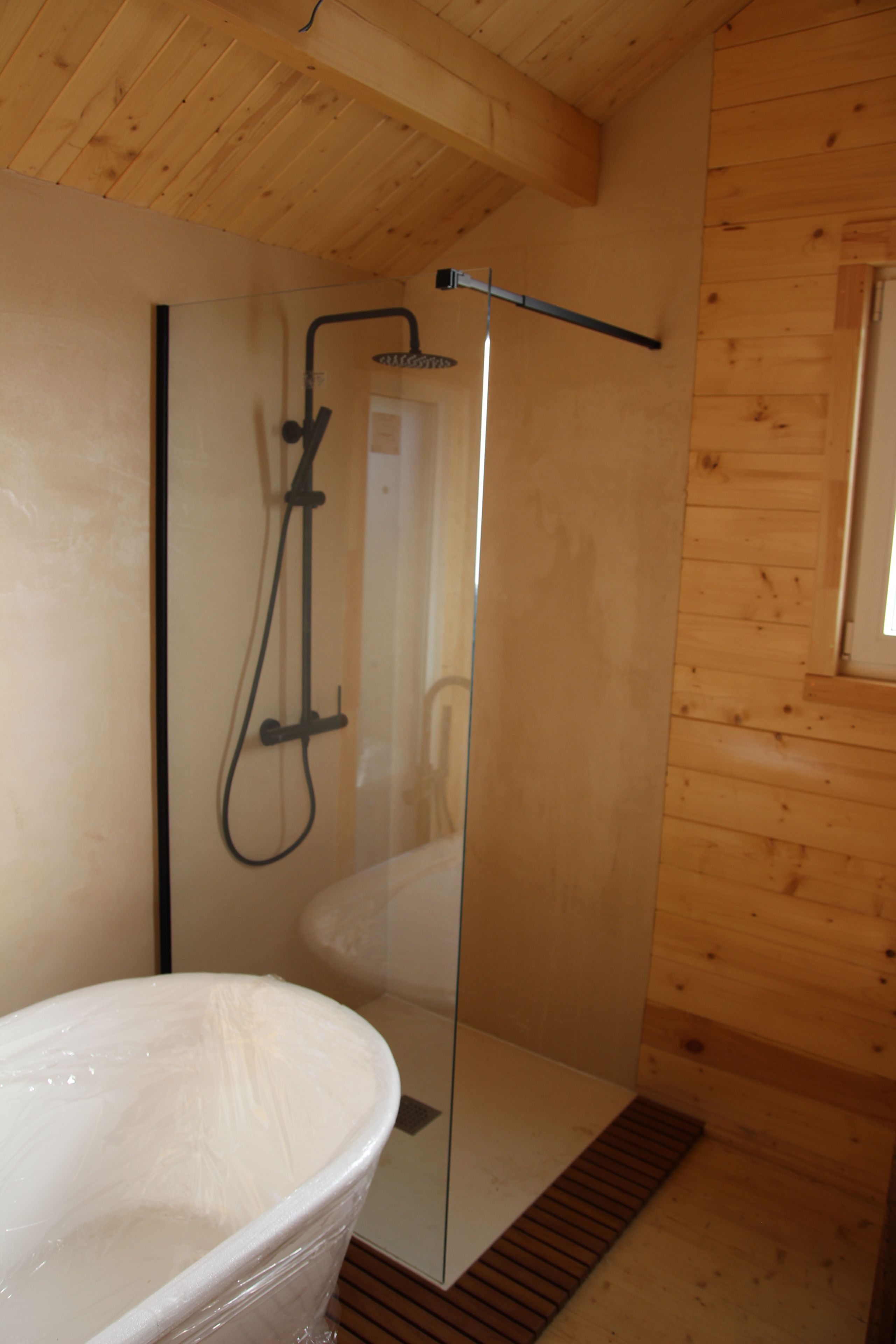 Een moderne badkamer met een douchecabine van glas, een vrijstaand bad en houten lambrisering.