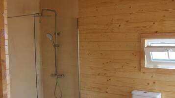 A wooden interior with a glass-enclosed shower, a toilet, and a window.