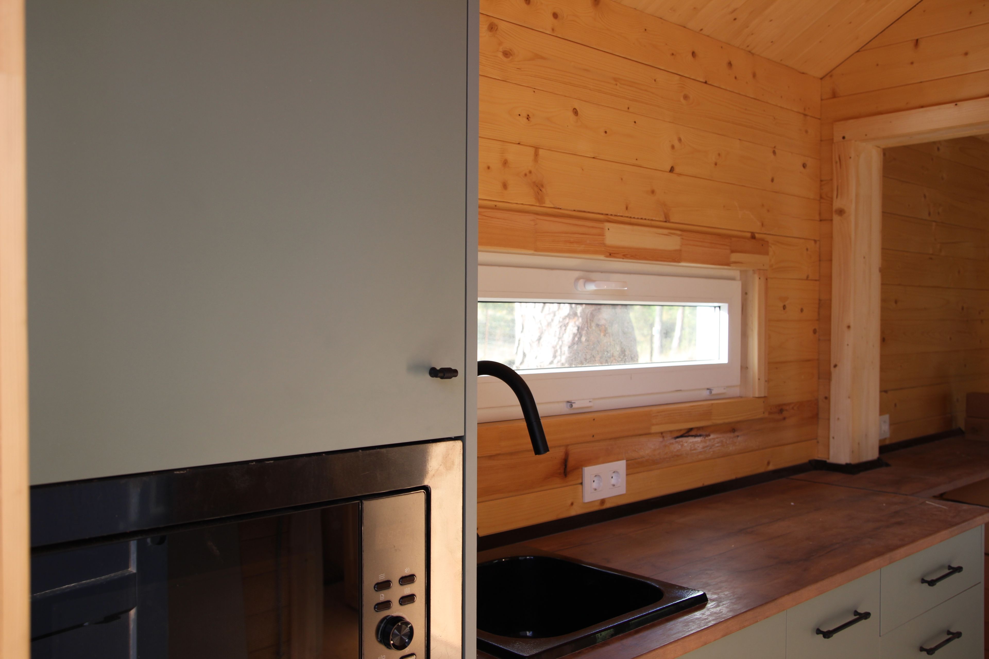 A kitchen with a window, wooden walls, a stainless steel sink, and a cabinet.