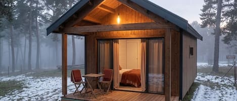 A wooden cabin with a glass door, a bed, and a small table with chairs.