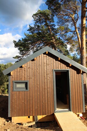 A small wooden cabin with a door and a window, surrounded by trees.