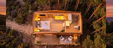 A wooden cabin with a deck, a sofa, a dining area, and a small kitchen.