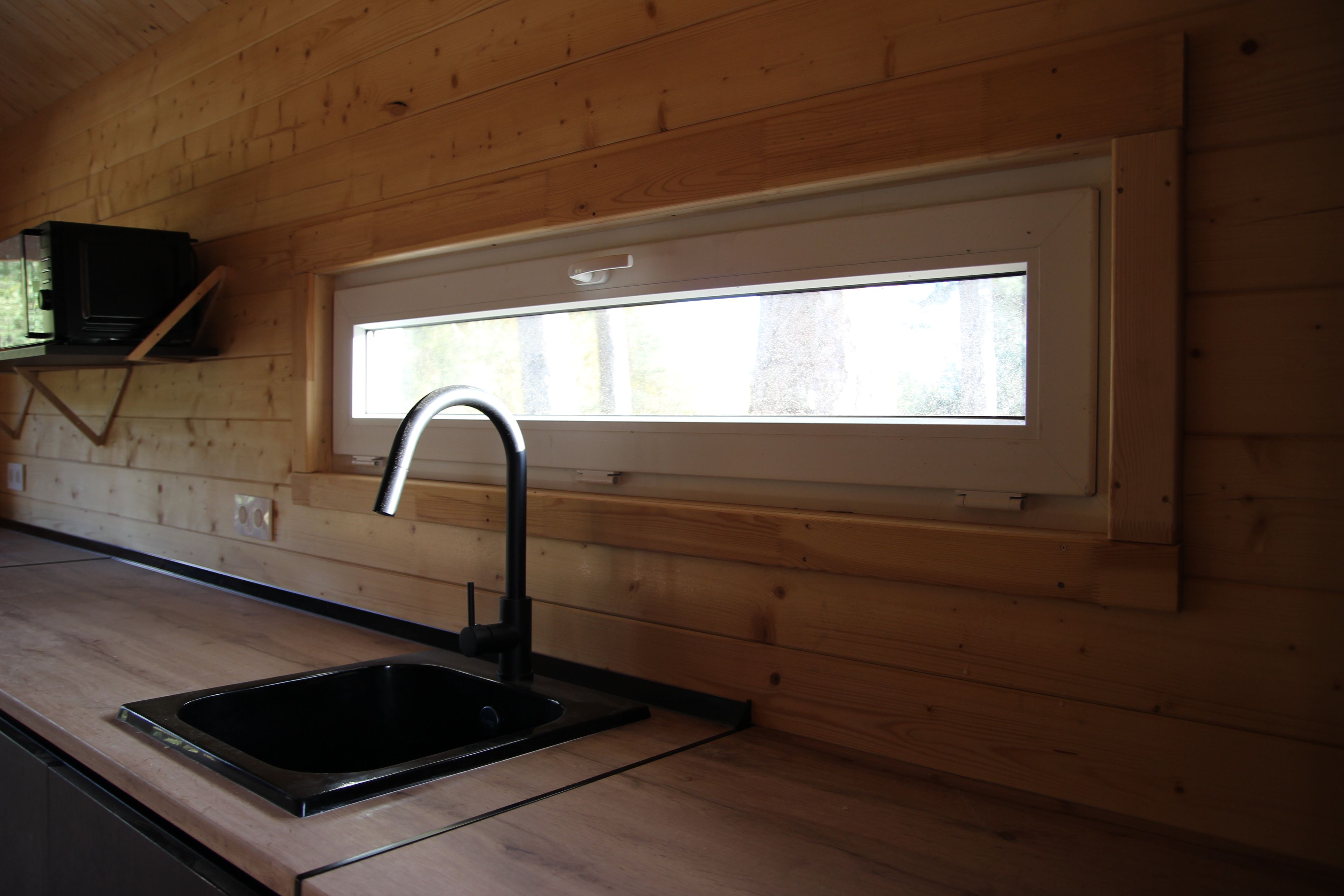 Een keuken met een zwart spoelbak, houten wanden en een raam boven de spoelbak.