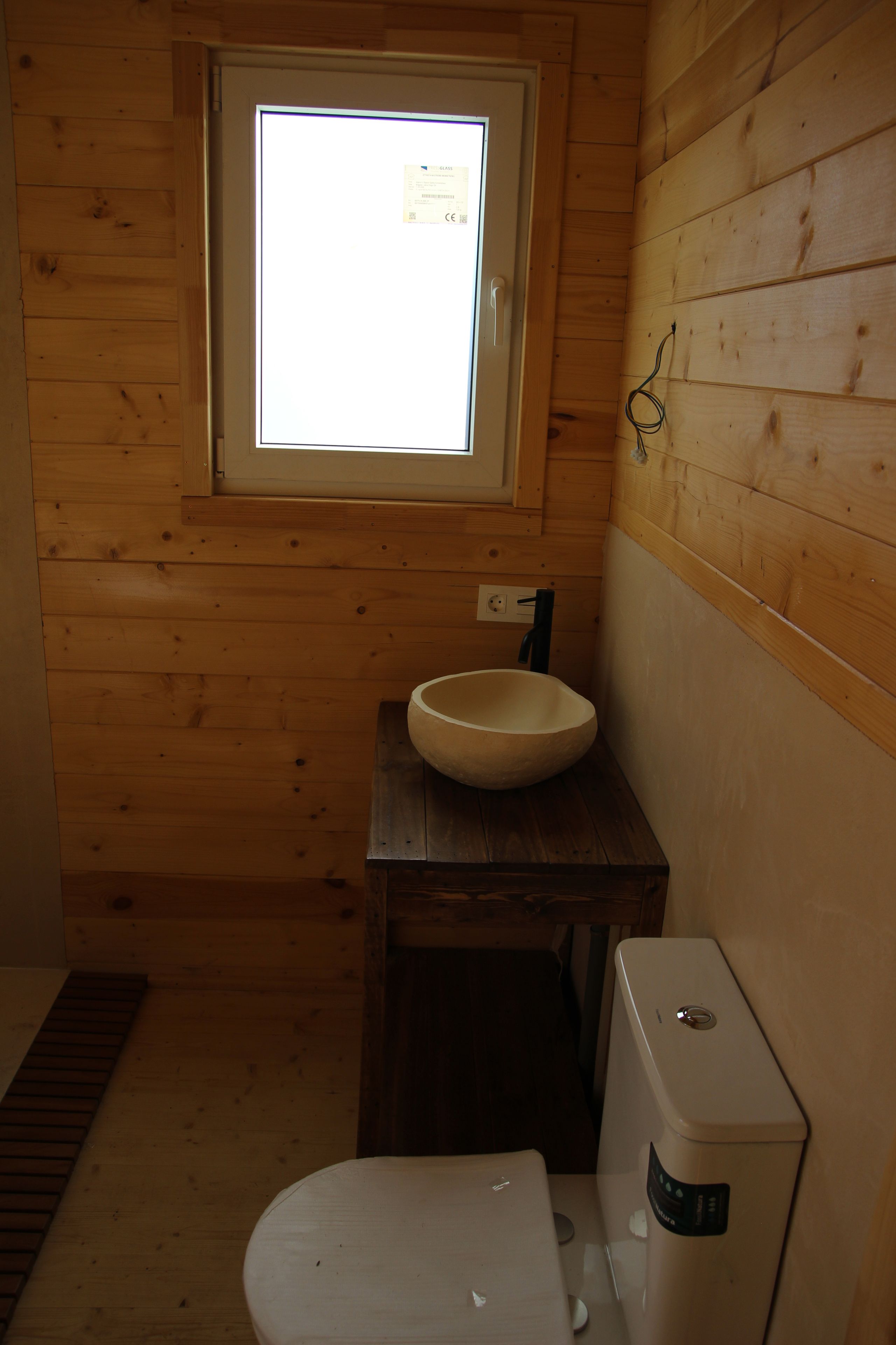 Une petite salle de bain en bois, avec une fenêtre, un lavabo et des toilettes.