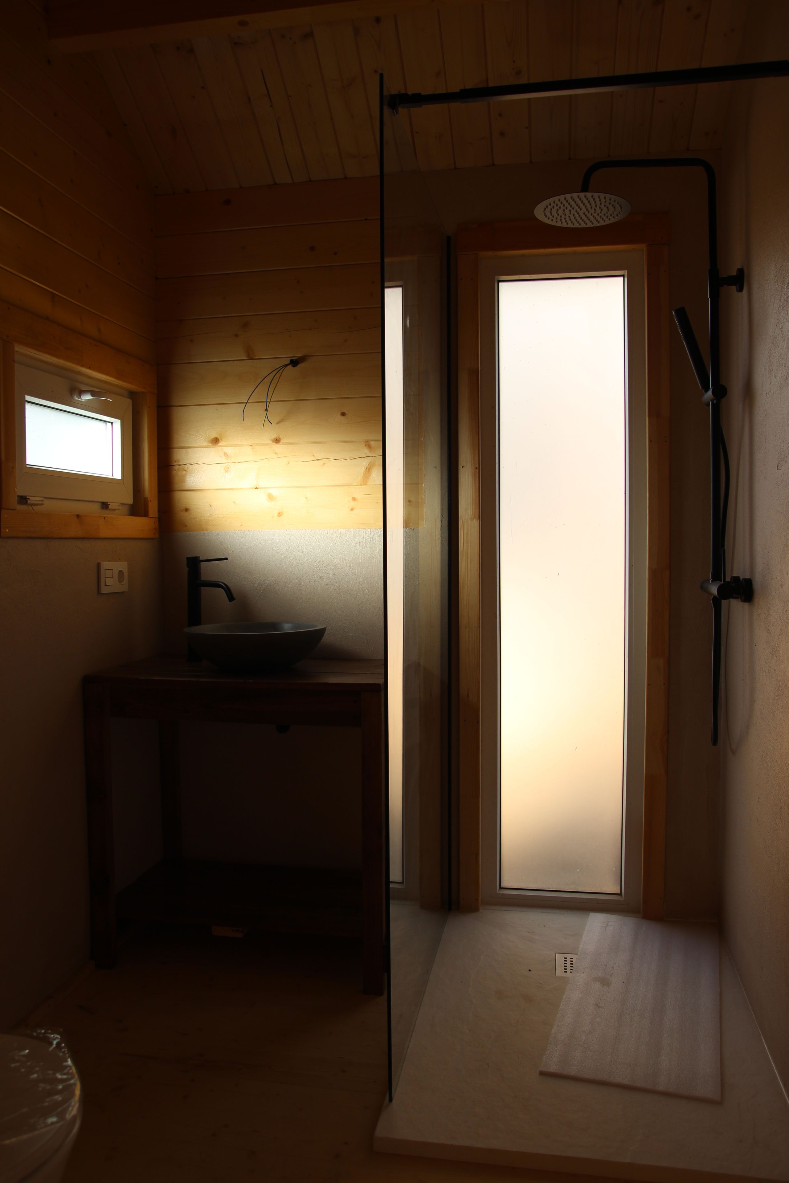 Une petite pièce à la lumière tamisée, avec un intérieur en bois, un évier et un espace douche.