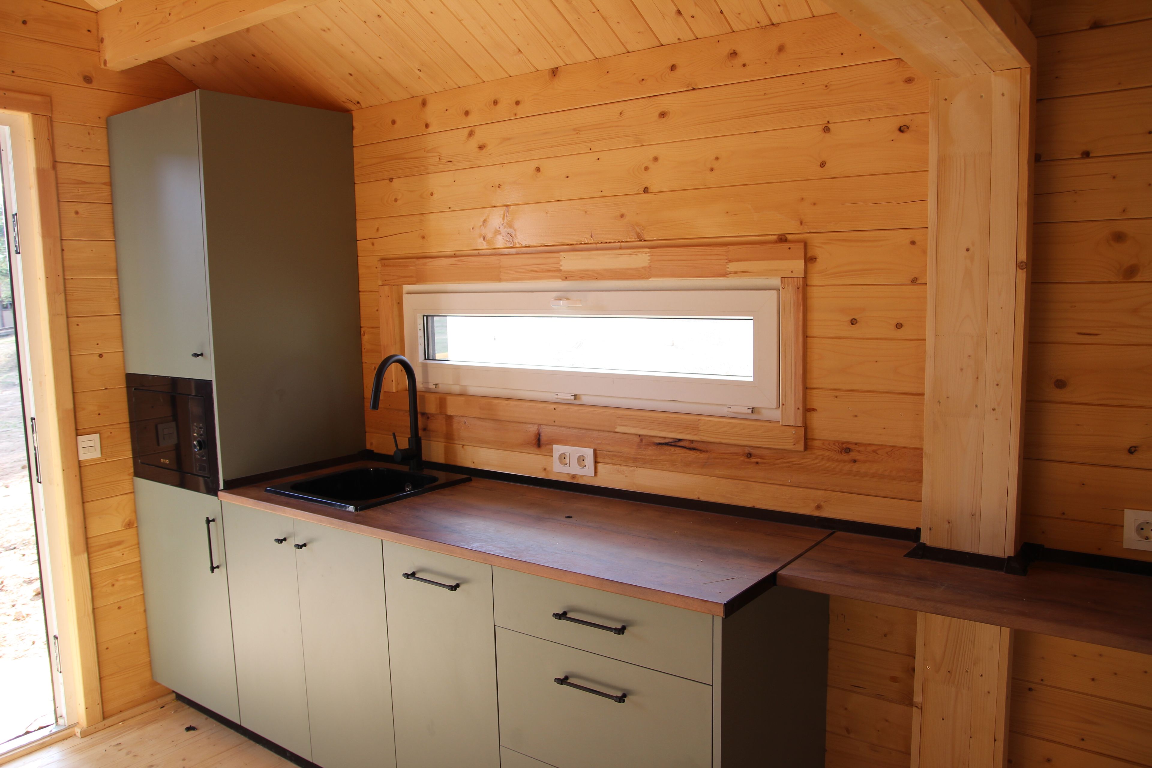 A compact kitchen with a built-in sink, a window above the countertop, and wooden cabinetry.