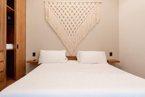 A bed with white bedding, two pillows, and a macramé wall hanging. - Luxury 2BR w/Rooftop Pool & Gym I Walk to Beach (Tulum)