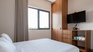 A hotel room with a bed, a TV mounted on the wall, and a wardrobe with a mirror. - Luxury 2BR w/Rooftop Pool & Gym I Walk to Beach (Tulum)
