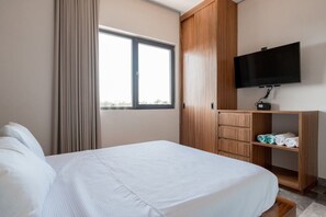 Ein Hotelzimmer mit Bett, einem an der Wand befestigten Fernseher und einem Schrank mit Spiegel.