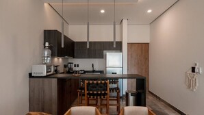 A modern kitchen with dark wood cabinetry, a central island with bar stools, and a dining area with a wooden table and chairs. - Luxury 2BR w/Rooftop Pool & Gym I Walk to Beach (Tulum)
