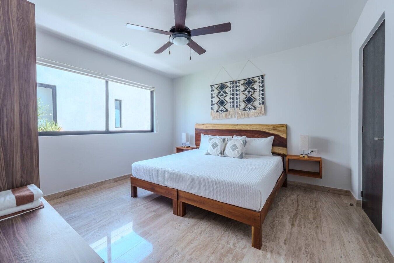 A bedroom with a wooden bed, a ceiling fan, a window, and a wall-mounted artwork.