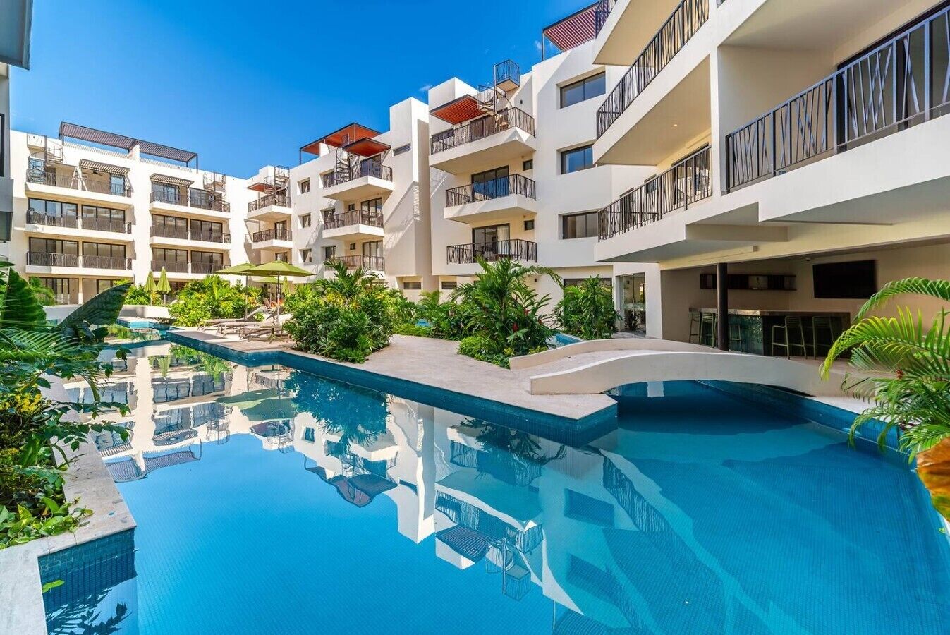 Un hôtel moderne doté d’une piscine centrale, de nombreux balcons et d’une végétation luxuriante.