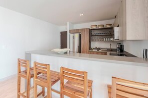 A modern kitchen with a central island, wooden chairs, and a stainless steel refrigerator. - Relaxing 2BR Oasis w/ Pool & Balcony | Sleeps 6 (Tulum)