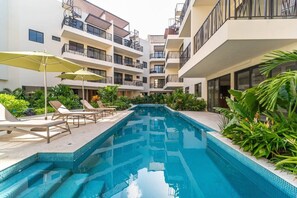 A swimming pool with lounge chairs and umbrellas, surrounded by multi-story buildings with balconies. - Relaxing 2BR Oasis w/ Pool & Balcony | Sleeps 6 (Tulum)