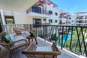 A balcony with wicker furniture, a small round table, and a view of a swimming pool. - Relaxing 2BR Oasis w/ Pool & Balcony | Sleeps 6 (Tulum)