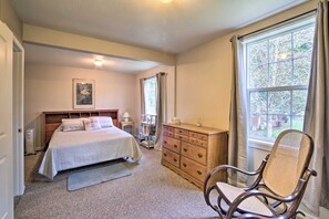 Ein Schlafzimmer mit Bett, Kommode, Stuhl und einem Fenster mit Vorhängen.