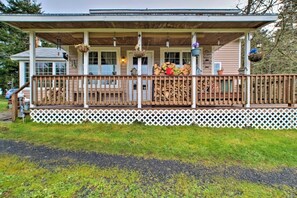 A wooden cabin with a porch, white lattice fence, and hanging flower baskets. - Coos Bay Farmhouse Near Ocean, Pet-Friendly (Coos Bay)